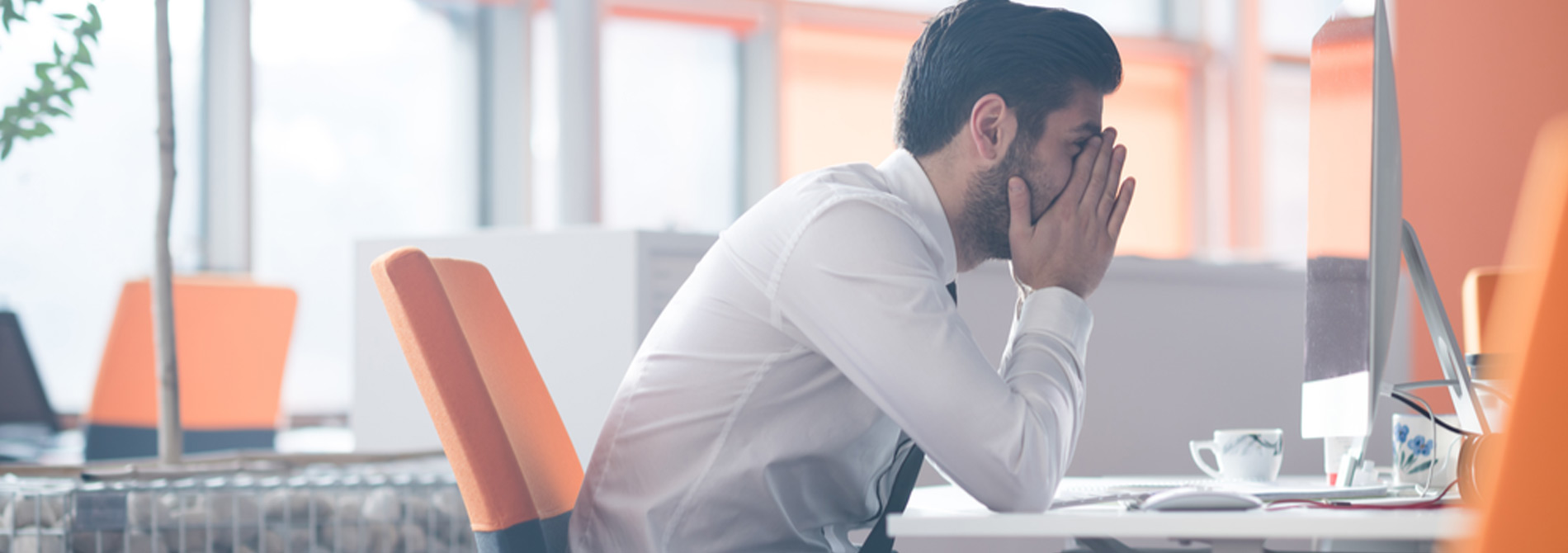 man sitting a desk holding head in hands