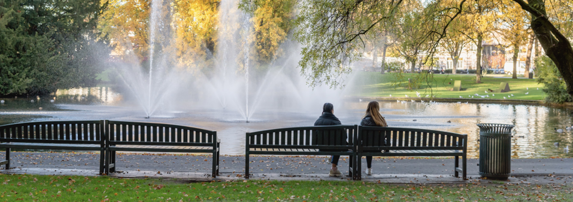 Two women sitting on park bench in front of fountains
